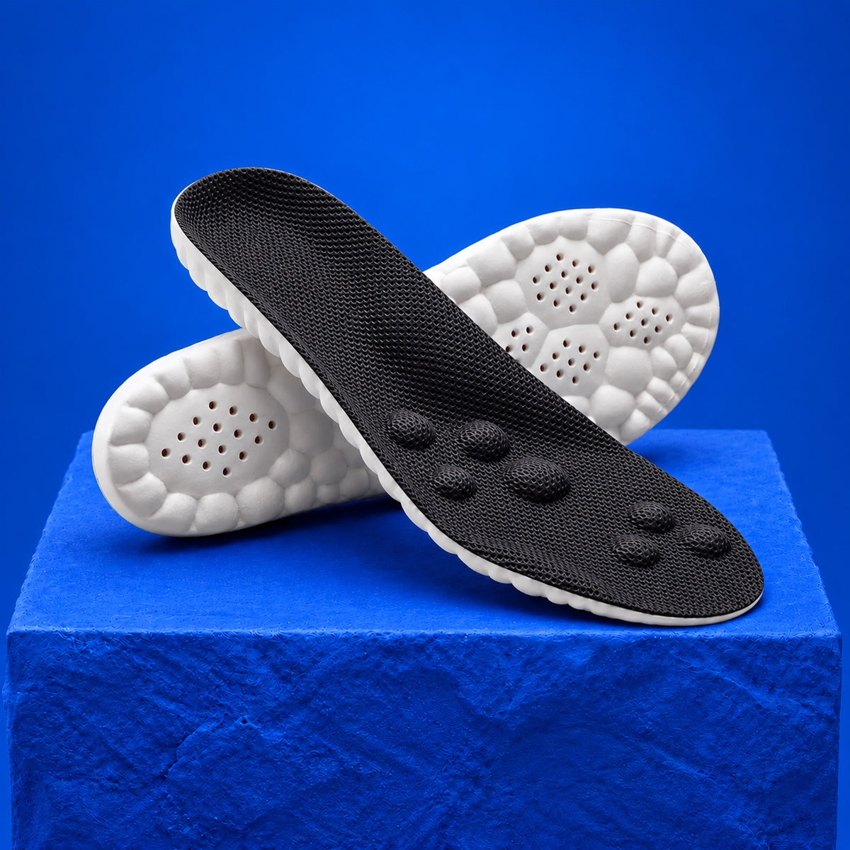 SoftInch Comfort Insoles in black: a crossed pair on a cobalt block, black mesh top and white cloud foam base